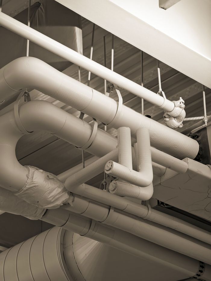 Home Complex network of industrial pipes and ducts in a sepia-toned indoor setting.