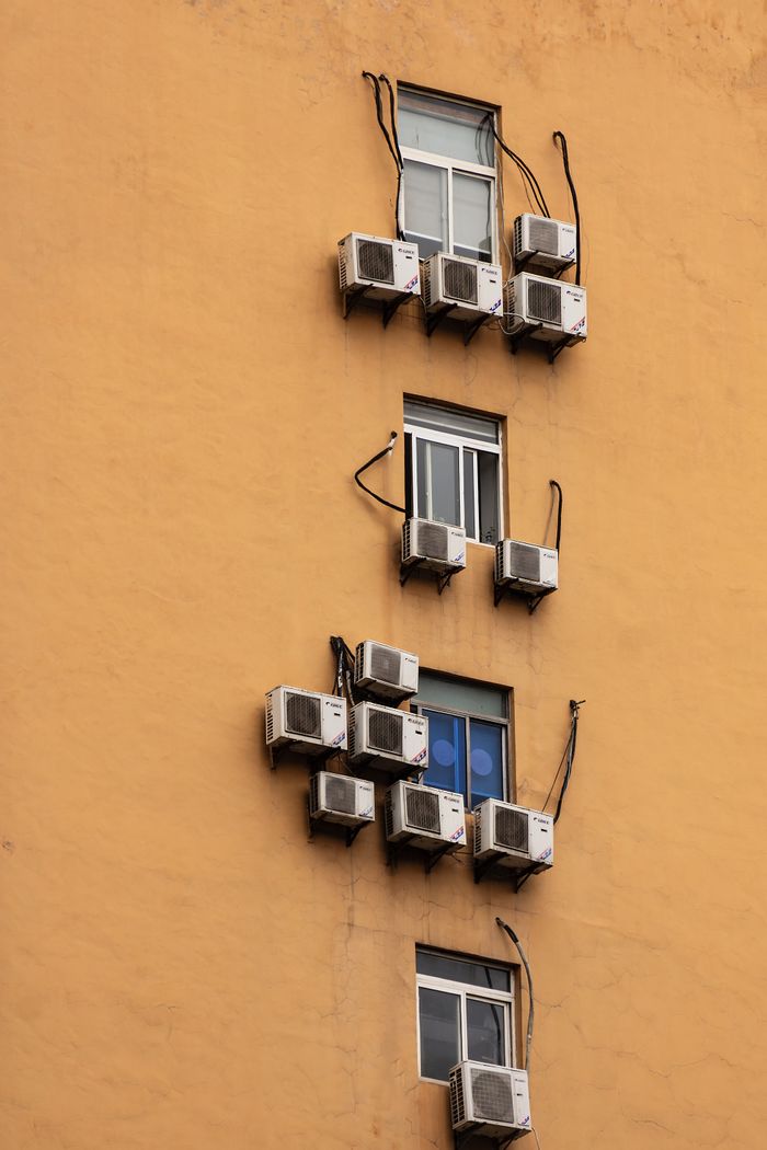 Yellow building facade with windows and numerous air conditioning units attached.